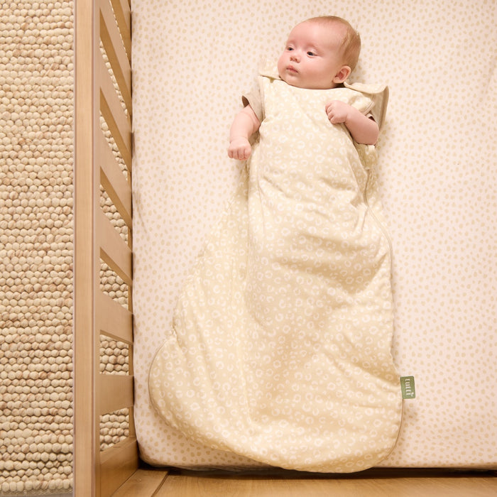 Baby lying in the Love Cats baby sleep bag in a wooden cot bed