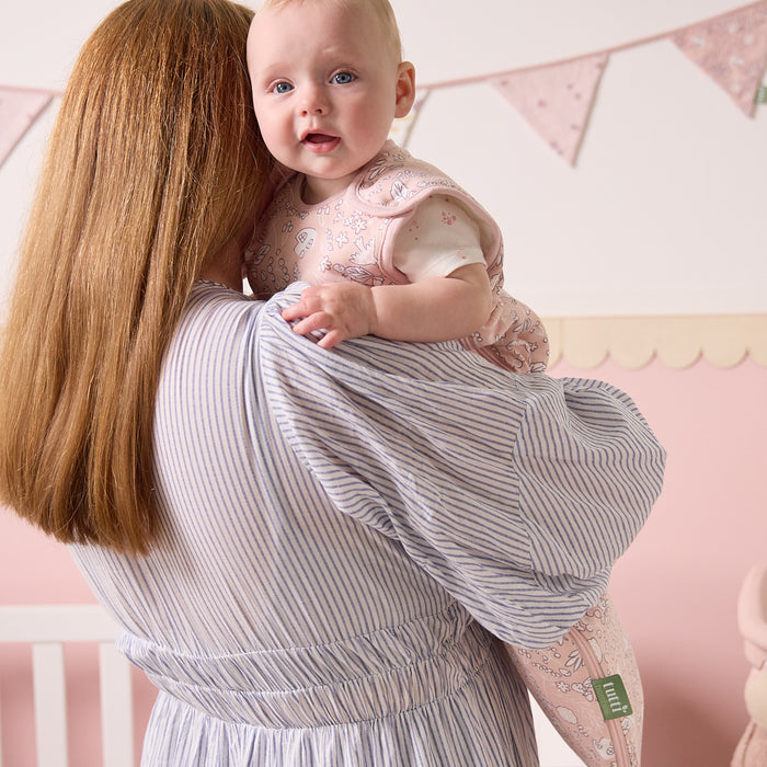Mother holding baby dressed in the Tiny Tails sleep bag, featuring a soft pink woodland print for cosy comfort and style