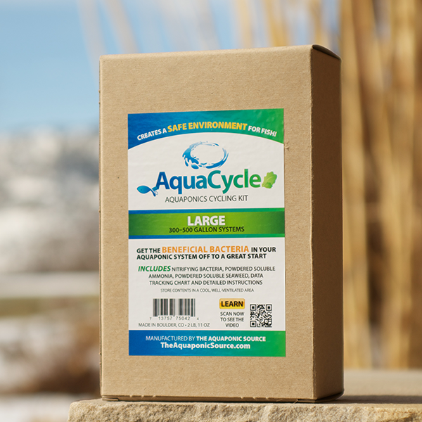 A brown box labeled "AquaCycle Fish-less Cycling Kit" by TAS sits outdoors with blurred plants and sky behind, ideal for aquaponic gardening and starting fish-less cycling with essential nitrifying bacteria.
