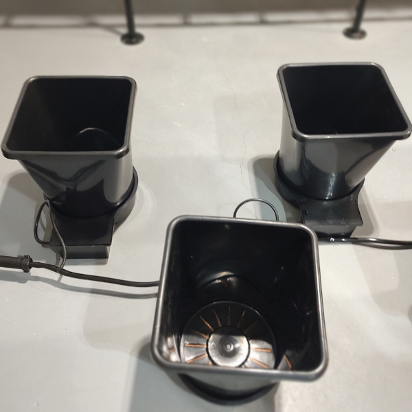 Three black TAS pots, including the AutoPot Bucket 1XL Module, 6.6 Gallon System, with tomato plants on a table next to each other.