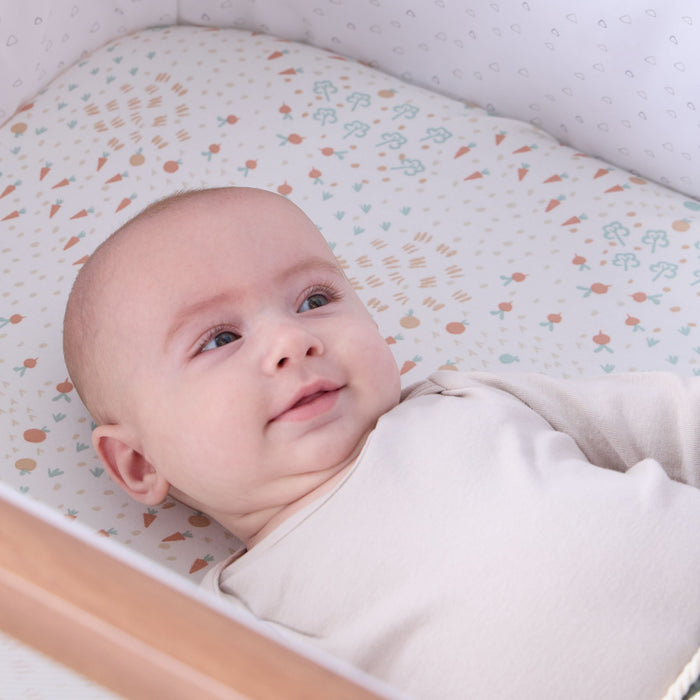 Baby lying in the CoZee next to me crib with a patterned fitted sheet