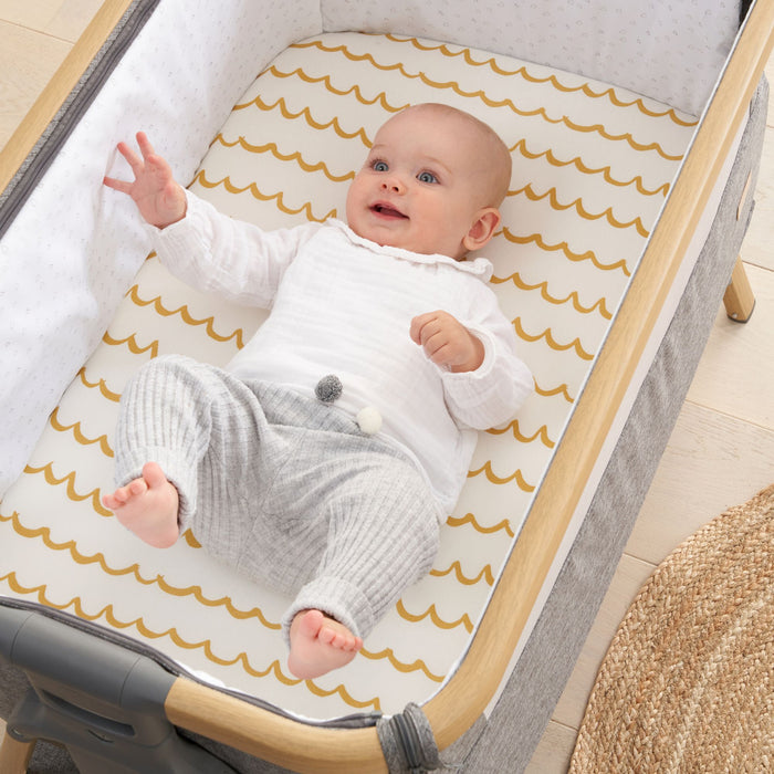 Baby lying in crib on Our Planet fitted sheet with mustard wave pattern, highlighting breathable organic cotton fabric and cosy design