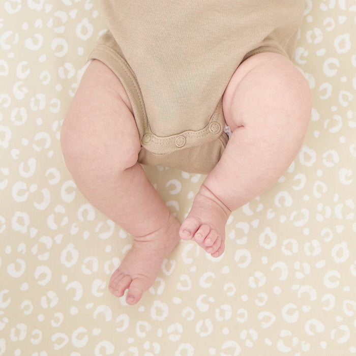 Close-up of baby’s legs resting on the Love Cats fitted sheet in soft beige with playful cat-inspired spots and gentle texture