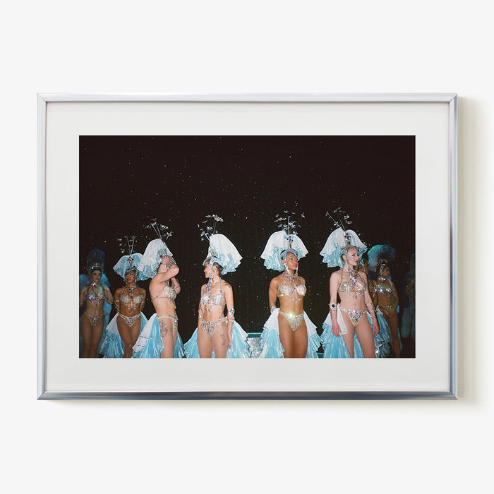 Framed photograph of several women in elaborate light blue and silver feathered costumes against a dark starry