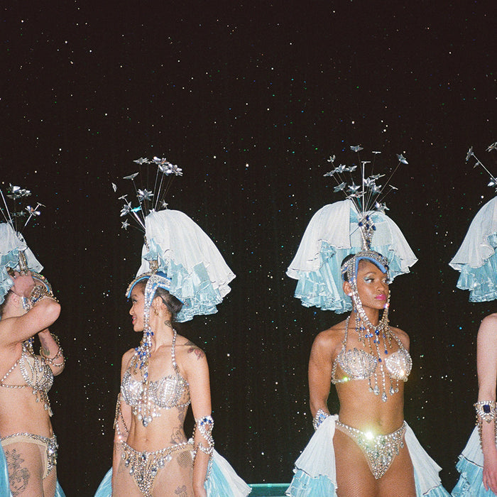 Close-up photograph of three women in sparkling light blue and silver costumes with feathered headpieces