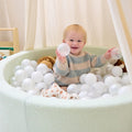 Smiling toddler playing inside the Bola baby ball pit in sea mist, holding soft balls during relaxed sensory playtime at home