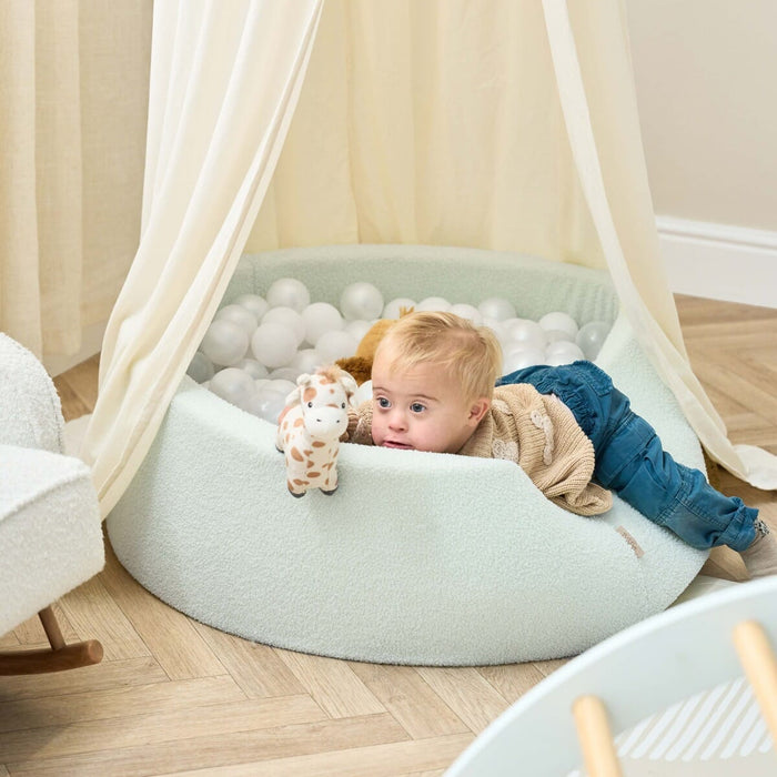 Baby lying comfortably over the padded edge of the Bola baby ball pit in sea mist, enjoying soft textures and sensory playtime
