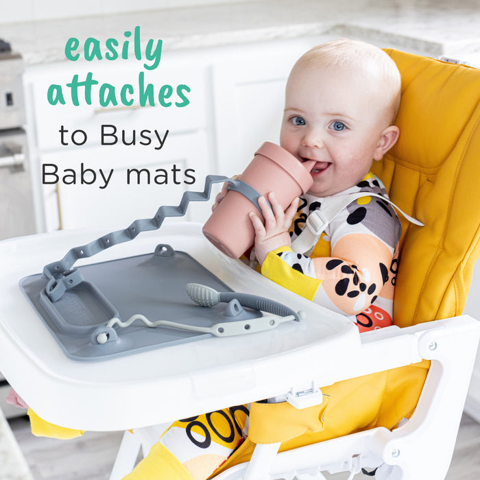 baby drinking out of cup smiling the cup attached with busy baby bottle bungee to busy baby original suction placemat