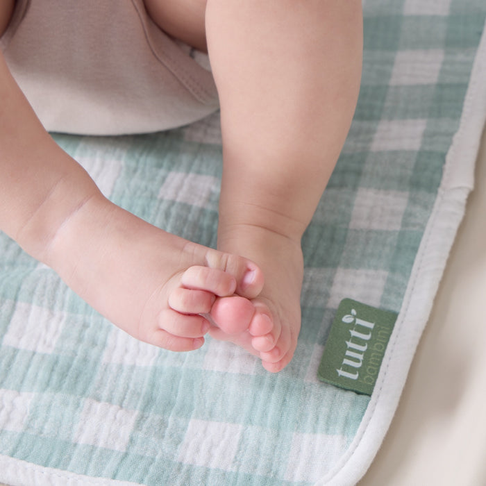 Baby feet resting on green gingham changing mat liner, highlighting its soft muslin texture and cosy, baby-friendly finish