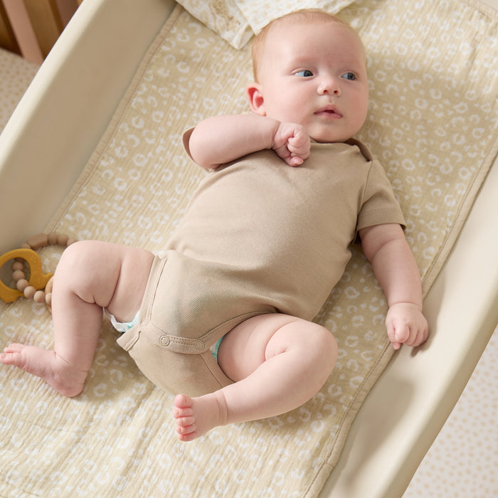 Baby lying comfortably on beige leopard print changing mat liner, highlighting the soft muslin fabric and calm, cosy nursery tones
