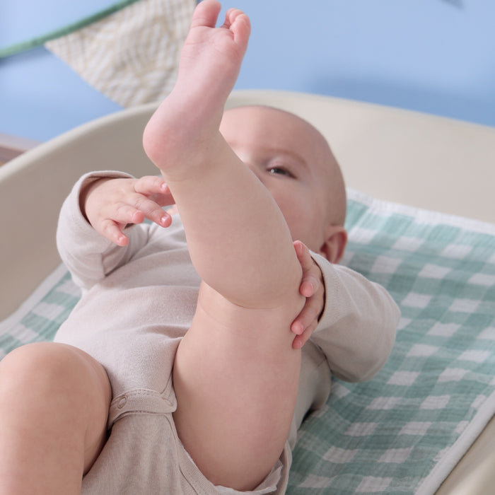 Baby lying on soft muslin changing mat liner in green gingham, showing its gentle texture and comfortable, breathable design