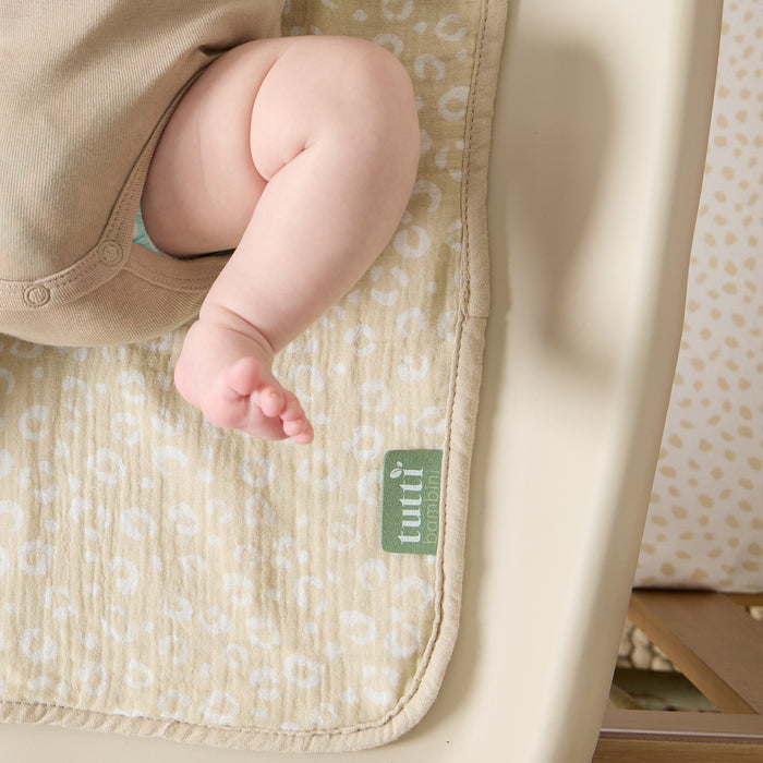Baby’s leg resting on soft muslin changing mat liner in beige leopard print, showing its gentle, absorbent texture and soft edges