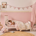 Child sleeping in a cot bed with floral bedding in a cosy bedroom setting.