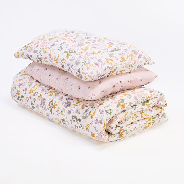 Floral woodland cot bedding set folded and stacked, featuring coordinating duvet cover and pillowcase in soft pastel tones.