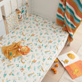 Lifestyle nursery view of the Run Wild cot bed fitted sheet with safari animal print, styled with toys and blankets for a playful, cosy space