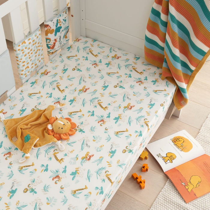 Lifestyle nursery view of the Run Wild cot bed fitted sheet with safari animal print, styled with toys and blankets for a playful, cosy space