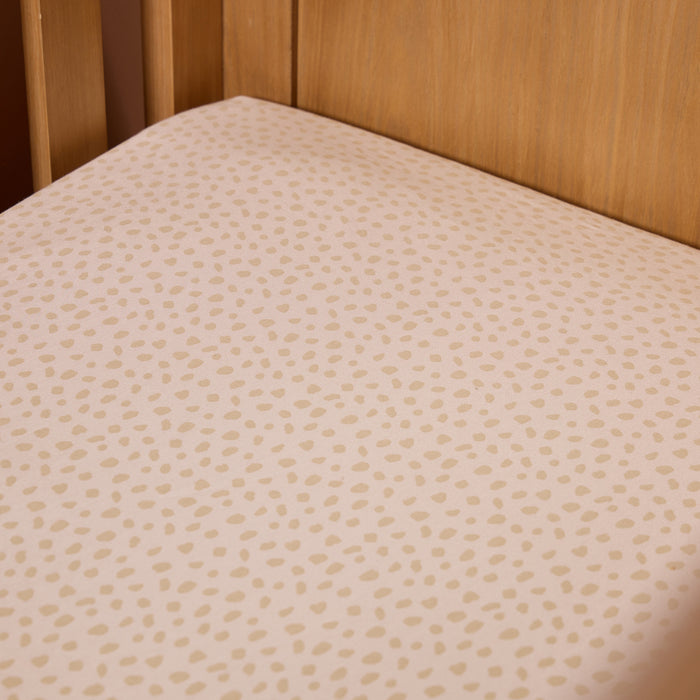Corner close-up of the Love Cats fitted sheet in soft beige with a playful spot print, styled neatly inside a natural oak cot.