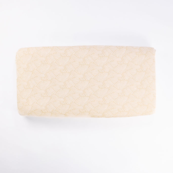 Cutout of Good Life cot fitted sheet in beige featuring a subtle hand-drawn wave pattern in white, crafted from soft, natural cotton fabric