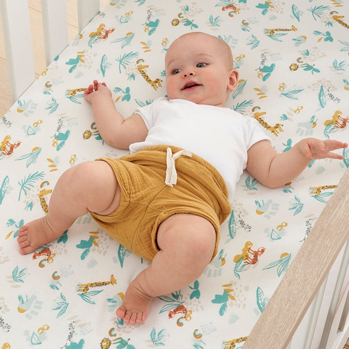 Baby lying on cot fitted sheet in Run Wild design, soft cotton with playful jungle animal prints for a cosy, breathable sleep