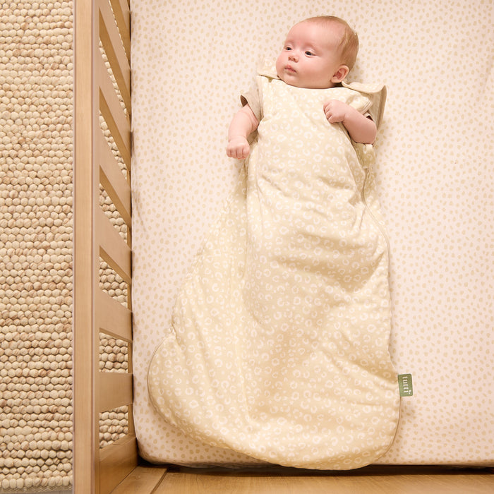 Overhead view of baby snuggly lying in a sleep bag and on the cot fitted sheet from our love cats collection.