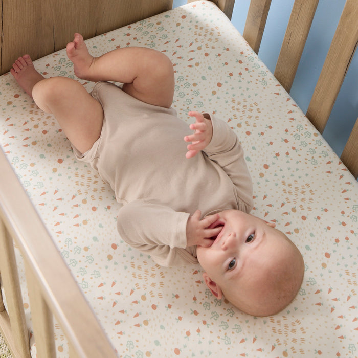 Baby lying on a cot bed with a patterned sheet from the Good Life collection