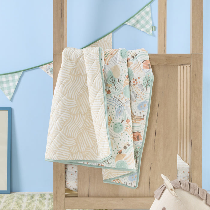 Good Life cot bed coverlet draped over cot rail, featuring reversible woodland and neutral stripe prints with soft green edging