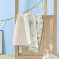 Good Life cot bed coverlet draped over cot rail, featuring reversible woodland and neutral stripe prints with soft green edging