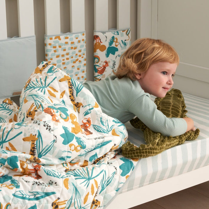 Toddler lying on cot with Run Wild coverlet, quilted cotton with colourful jungle animal prints creating a cosy, playful sleep space