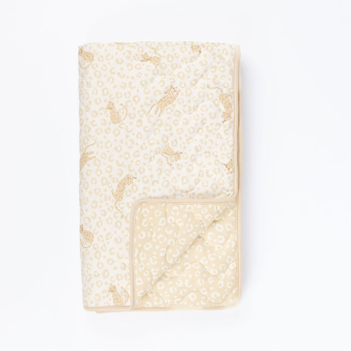 Cutout view of Love Cats cot bed coverlet showing reversible leopard and print design, with soft beige tones and piped edging