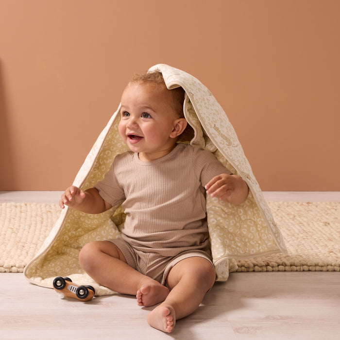 Smiling baby playing under the Love Cats cot bed coverlet, wrapped in soft quilted layers with a charming neutral animal pattern