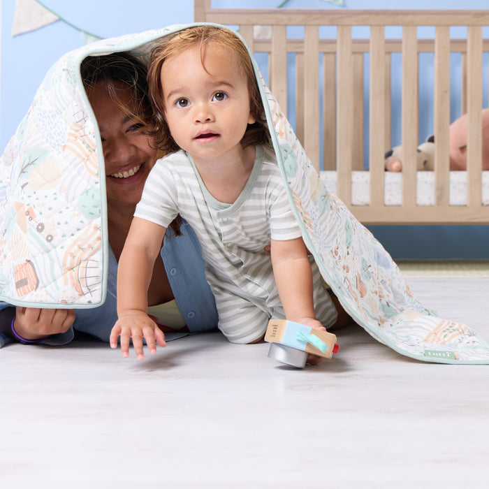 Parent and toddler sharing a playful moment beneath the Good Life cot bed coverlet, showcasing its soft texture and calming colours