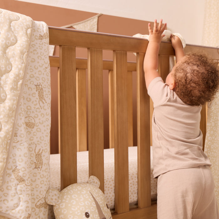 Love Cats cot bed coverlet draped over wooden cot rail, showcasing reversible leopard print design in soothing neutral tones