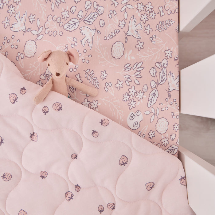 Close-up of Tiny Tails cot bed coverlet with storybook mouse toy on top, highlighting soft pink floral and strawberry print details