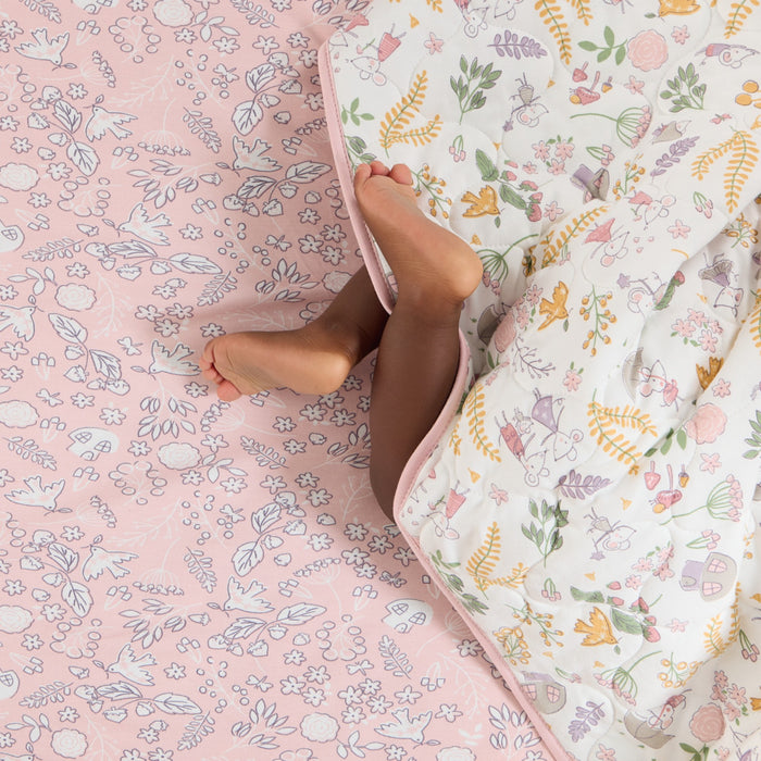 Toddlers feet peeking from beneath the Tiny Tails cot bed coverlet, showing reversible pink floral print design