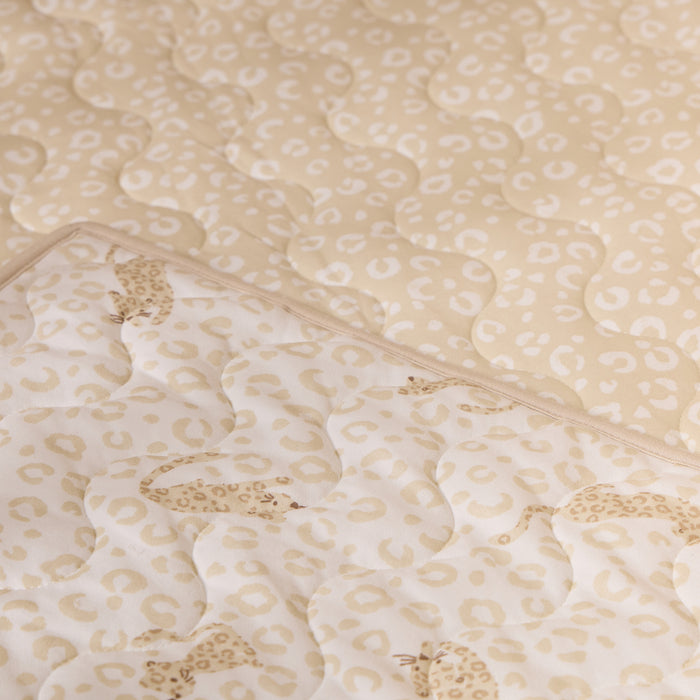 Close-up of the Love Cats cot bed coverlet showing soft quilted texture and reversible beige leopard print design