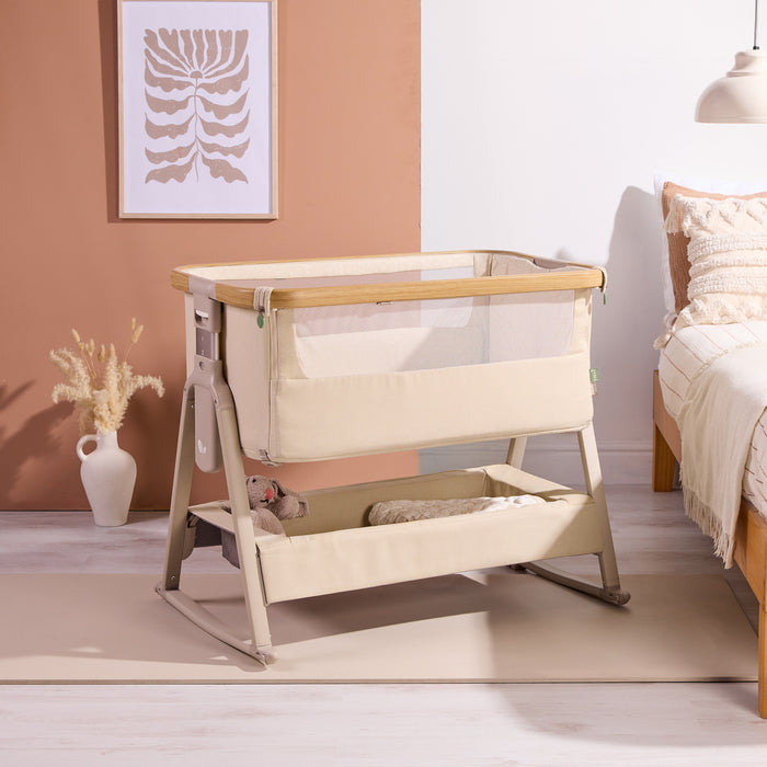 Styled nursery scene featuring the CoZee Air 2 bedside crib in toasted oak/sand with soft textiles and calm, neutral tones.