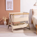 Styled nursery scene featuring the CoZee Air 2 bedside crib in toasted oak/sand with soft textiles and calm, neutral tones.