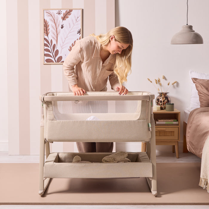 Lifestyle image of a parent leaning over the CoZee Air 2 in cocoa, highlighting easy access, mesh panels and everyday bedside use.