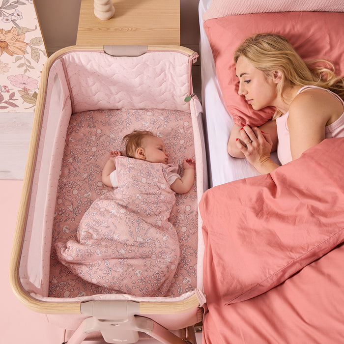 Overhead view of baby resting in the CoZee Air 2 bedside crib in blush, positioned securely alongside the parent’s bed.