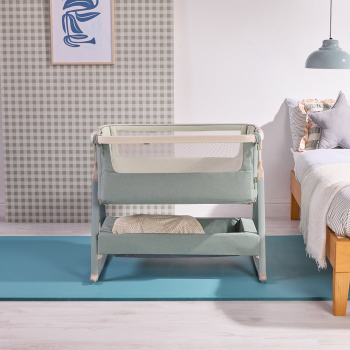 Front room view of the cozee air 2 bedside crib in kelp, styled beside the bed to showcase breathable mesh sides.
