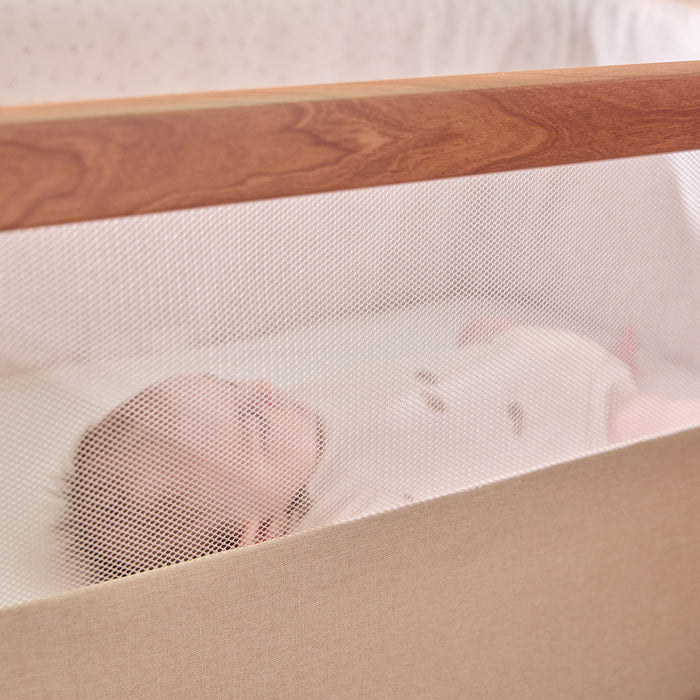 Baby sleeping peacefully inside the CoZee bedside crib in Scandinavian Ecru, viewed through the breathable mesh side for visibility and airflow