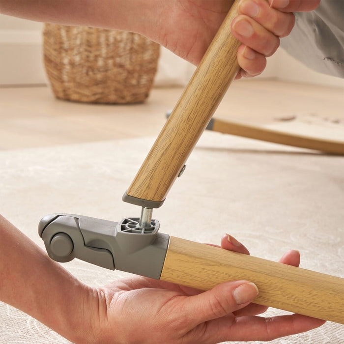 Close-up of hands connecting CoZee rocking bars in oak, demonstrating simple and secure assembly for rocking crib mode