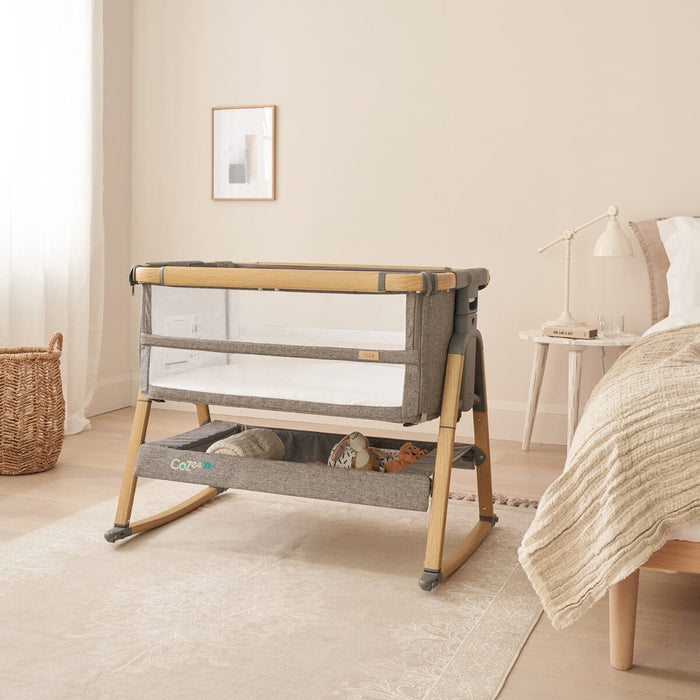 Room view of the CoZee bedside crib in oak and charcoal with attached rocking bars, blending natural tones with practical comfort