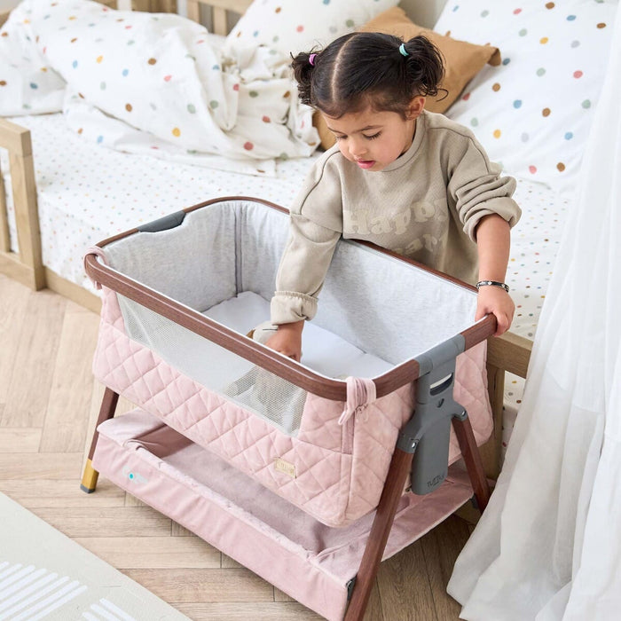Child reaching into the CoZee Luxe Mini Me crib in walnut and blush, showing the low height and toddler-friendly proportions