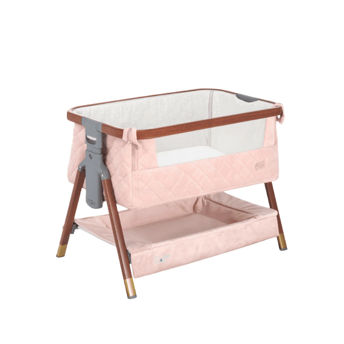 Angled view of the CoZee Luxe Mini Me crib in walnut and blush finish, highlighting the compact design, mesh sides, and easy-access base