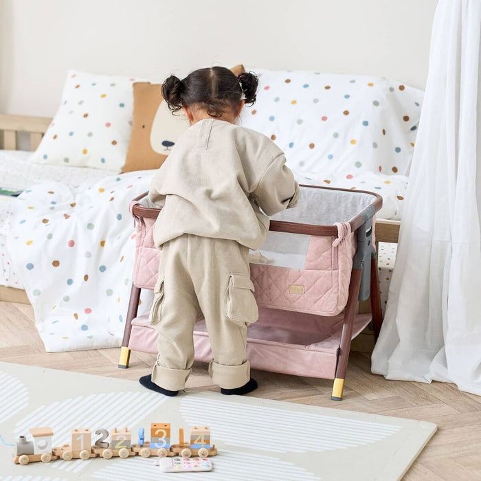 Child interacting with the CoZee Luxe Mini Me crib in walnut and blush, showcasing playful scale and room-friendly styling