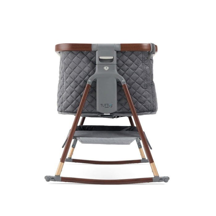 Side view of the CoZee Luxe bedside crib in walnut and slate with rocking bars attached, showing breathable mesh and compact frame