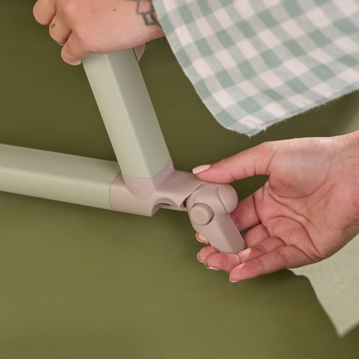 Close-up of the cozee air 2 bedside crib in eucalyptus showing the brake locking mechanism.