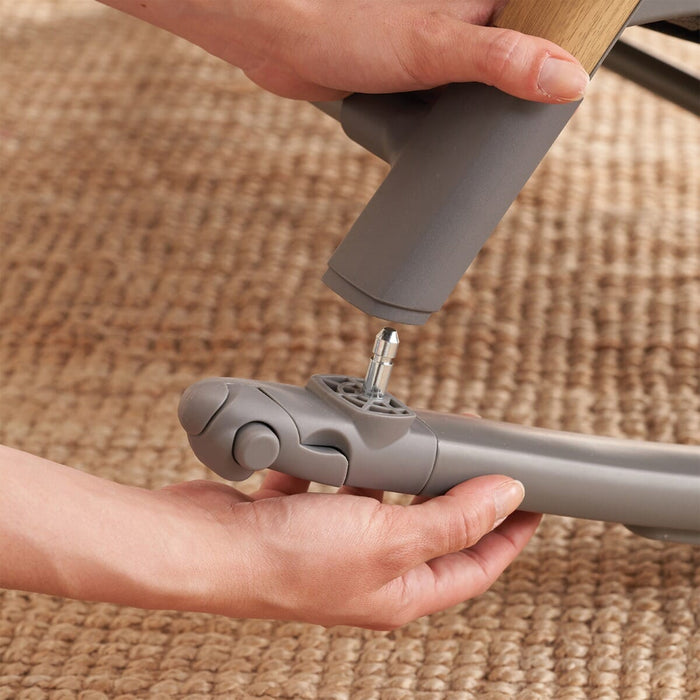 Hands attaching rocker bar to the CoZee bassinet leg, showing tool-free setup and secure click-in design for converting to rocking mode