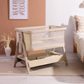 CoZee Zen bedside crib in sand with breathable mesh sides and under-crib storage shelf, styled in a calm neutral bedroom.